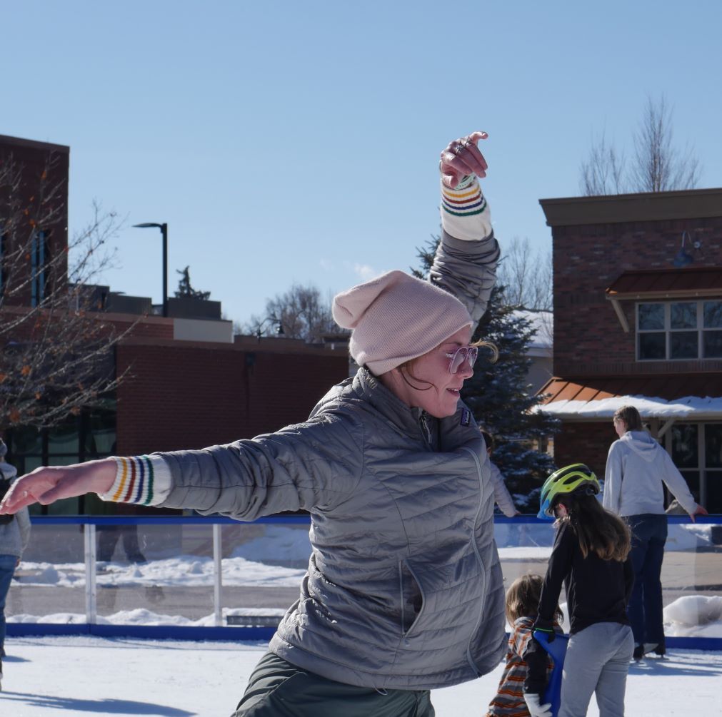 A woman figure skating on ice on a sunny day in a downtown area.
